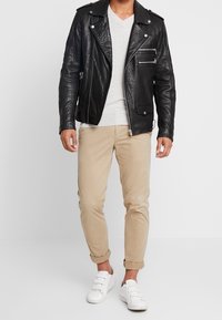 Veste de motard en cuir noir avec des accessoires en argent, associée à un pull léger gris clair, un chino beige retroussé et des baskets blanches.