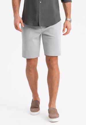 Shorts grises clairs en tissu tissé, offrant une coupe décontractée et une texture lisse. Associés à des chaussures brunes à enfiler.