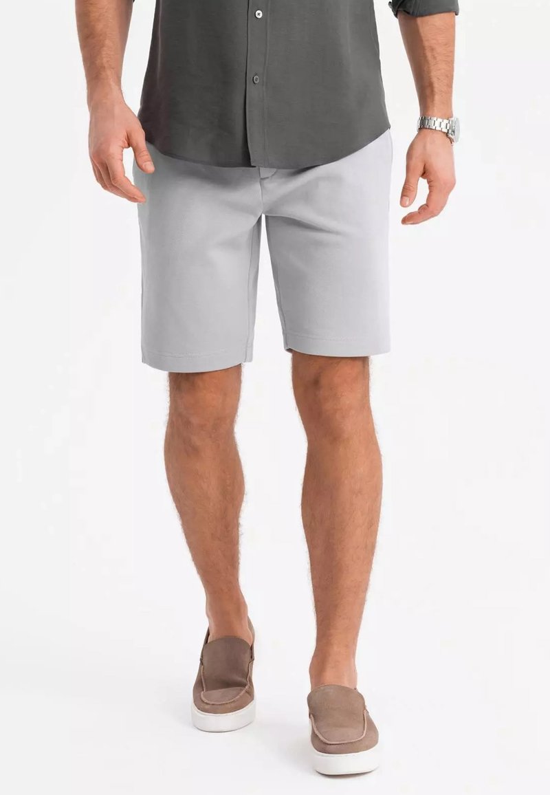 Shorts grises clairs en tissu tissé, offrant une coupe décontractée et une texture lisse. Associés à des chaussures brunes à enfiler.