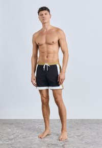 Čierne plavkové šortky s bielymi a zlatými akcentmi, s nastaviteľným pásom na šnúrku a pohodlným strihom. Hladká textúra a dĺžka do polovice stehna.