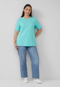 Een lichtgroene t-shirt met korte mouwen en een ronde hals, gecombineerd met losse blauwe jeans en witte sneakers. Eenvoudig ontwerp en casual pasvorm.