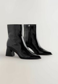 Černé kotníkové boty s lesklým koženým povrchem. Design s špičatou špičkou, středně vysokým blokovým podpatkem a bočním zipem pro snadné obouvání.