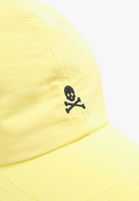 Yellow baseball cap made of fabric with a black embroidered skull and crossbones design on the front. Visible stitching details.