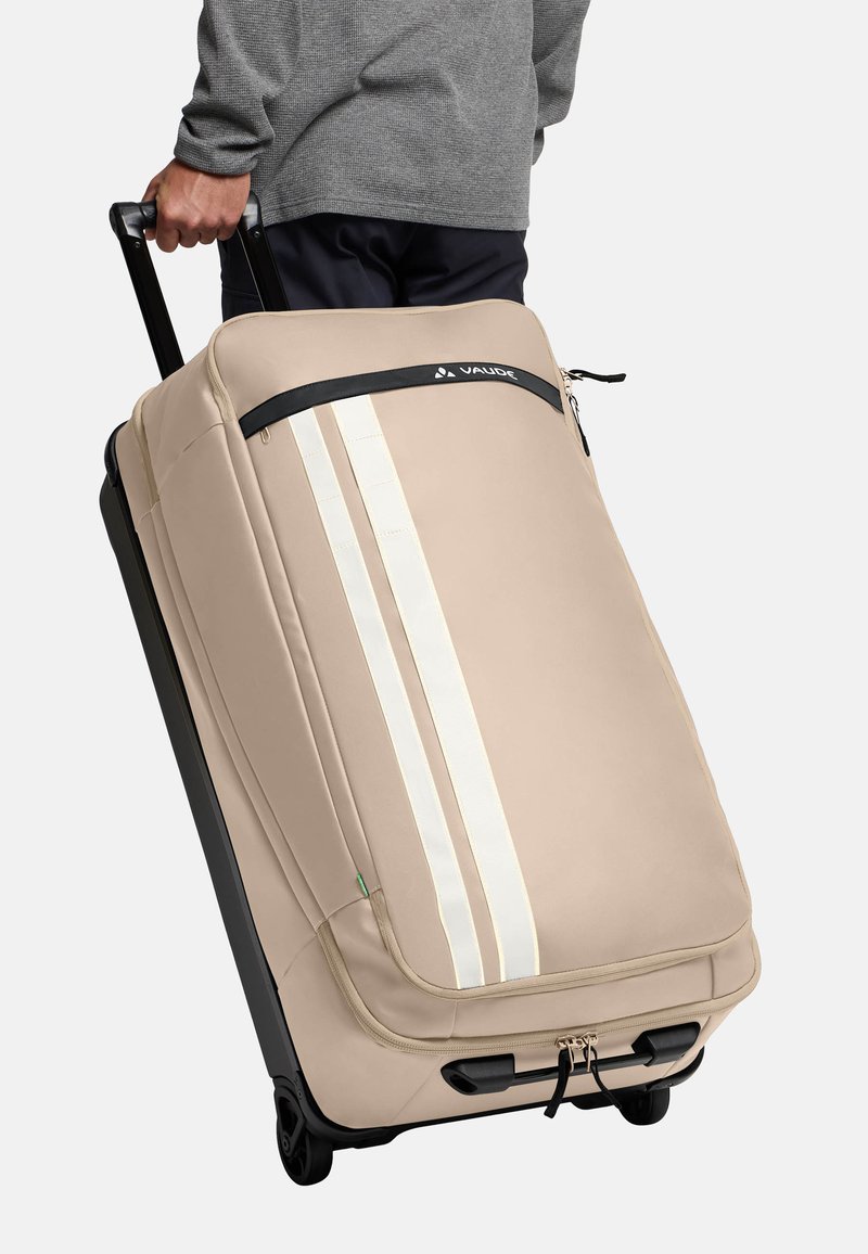 Beige koffer met wielen en witte strepen, gemaakt van duurzaam materiaal. Voorzien van een handvat aan de bovenkant, een ritsluiting en een stevige zwarte basis met wielen.