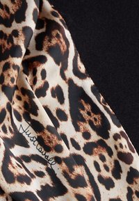 Sciarpa con stampa leopardata caratterizzata da una texture setosa, tonalità di marrone e nero, con un logo scritto a mano sul tessuto.