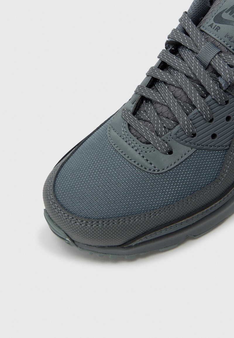 Gray sneaker with textured fabric upper, smooth leather accents, and thick sole. Features gray laces and visible stitching details.