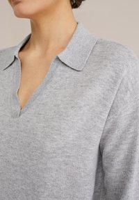 Harmaa neulepaita, jossa on kauluskalli ja V-aukko. Tekstuuri on pehmeä, hieman heatheroidulla viimeistelyllä.