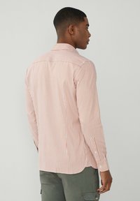 Chemise légère à manches longues avec des rayures verticales orange et blanches. Dotée d'un col boutonné et d'un ourlet arrondi avec des coutures accentuées.