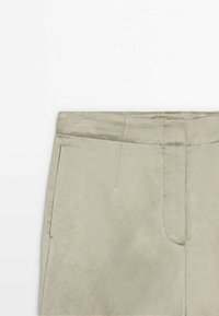 Vêtement beige avec couture avant, poche latérale et coutures de ceinture, présenté sur un fond blanc.