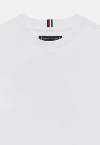 Weißes Baumwoll-T-Shirt mit Rundhalsausschnitt. Verfügt über ein Etikett mit "TOMMY HILFIGER"-Markierung und einem dekorativen rot-weiß-blauen Streifen am Hals.