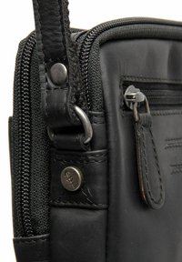 Borsa nera in pelle con un pannello in tessuto testurizzato, dotata di una tasca con zip, hardware in metallo e dettagli di cucitura in contrasto.