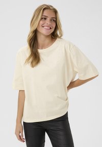 Cremefarvet bomulds t-shirt med rund halsudskæring og korte ærmer, pyntet med små, klare rhinsten spredt over stoffet.