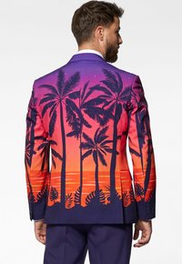 Blazer colorido con un diseño de atardecer y palmeras en tonos de púrpura, naranja y azul marino. Textura suave con patrones gráficos detallados.