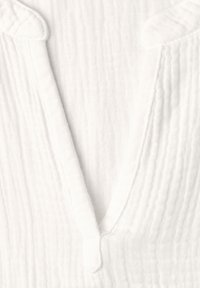 Tissu gaufré blanc texturé avec une ouverture en V profonde et un détail discret de col.