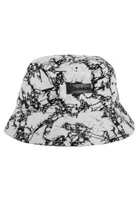 Svart och vit bucket hat med ett splattermönster, tillverkad av tyg, med en rektangulär logopatch på ena sidan.