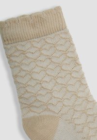 Calcetín beige de punto con un patrón de corazón, puño acanalado y textura suave. Presenta puntera y talón reforzados para mayor durabilidad.