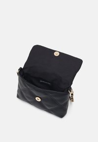 Černá prošívaná kožená taška se zlatým zapínáním na cvoček a řetízkovým popruhem, s černou látkovou vnitřní částí a štítkem.