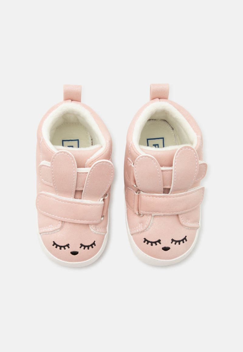 Chaussures bébé roses douces avec oreilles de lapin et broderie d'œil fermé, avec des sangles velcro et des intérieurs blancs rembourrés.