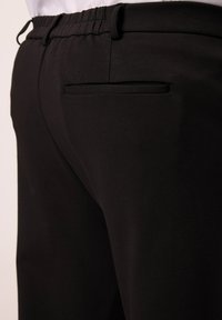 Pantalones negros con cinturilla elástica y textura suave, que cuentan con un bolsillo posterior y un corte relajado. Diseño minimalista, sin adornos visibles.