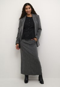 Hallhallane tweed-sülearvest musta peplum-ülaosa, kombineeritud sobiva halli seelikuga. Mustad kontsakingad täiendavad riietust. Sile tekstuur ja hästi istuv lõige.