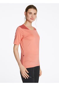 Camisa atlética de manga corta en coral claro con escote cuadrado, textura suave, patrón de olas sutil y acento de malla en contraste en los hombros.