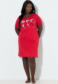 Rotes Baumwollkleid mit kurzen Ärmeln und V-Ausschnitt, mit einem Blumenmuster aus weißen Gänseblümchen und schwarzen Akzenten über der Brust.