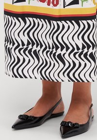 Sorte patentlæder slingback flats med spidse tæer og sløjfe accenter, parret med en sort og hvid bølget mønstret nederdel.