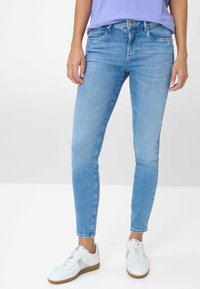 Jean skinny bleu clair en denim, dotés de cinq poches, d'une fermeture à bouton sur le devant, et d'un léger délavage pour un look épuré.
