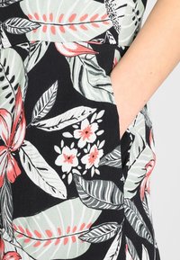 Tissu à motif floral présentant des feuilles vertes et des fleurs rouges sur un fond noir ; comprend une poche latérale visible.