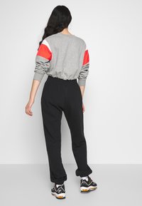 Gray sweatshirt with red and white striped accents on sleeves, paired with black sweatpants, and black sneakers with orange details.