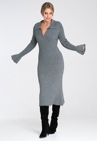Szara dzianinowa sukienka z prążkowanej tkaniny, z kołnierzykiem, długimi rękawami i rozszerzanymi mankietami, zestawiona z czarnymi kozakami do kolan.
