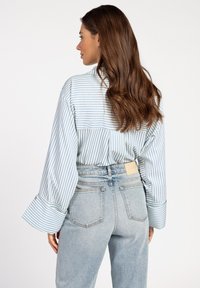 Striped blue and white shirt with wide sleeves, paired with light-wash jeans featuring a rear label and classic jean pockets.