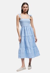 Vestido midi azul en capas con un cuerpo smock y tirantes atados. Presenta patrones de ojales y una tela ligera y fluida.