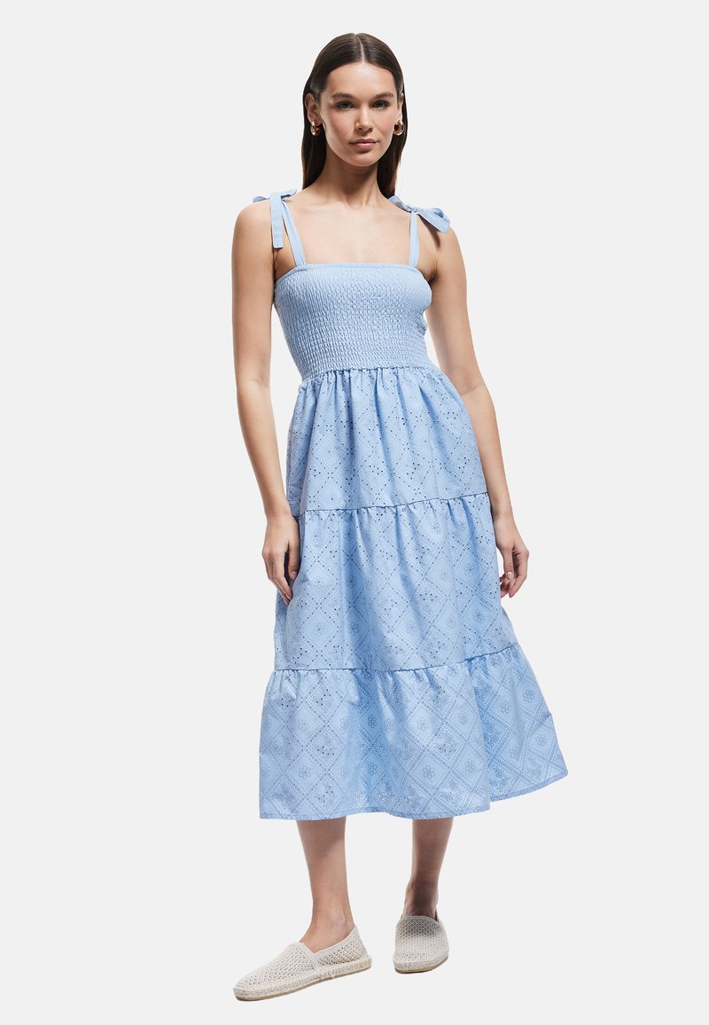 Vestido midi azul en capas con un cuerpo smock y tirantes atados. Presenta patrones de ojales y una tela ligera y fluida.