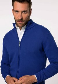 Blauer gestrickter Reißverschluss-Pullover mit hohem Kragen, gerippten Bündchen und Saum, der eine glatte Textur und ein elegantes Design aufweist.
