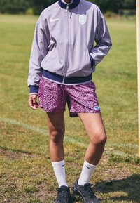 Nike gray bomber jacket with navy accents, pink leopard print shorts, white crew socks, and black athletic shoes on grass.