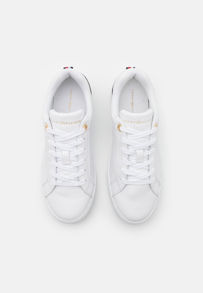 Weiße Leder Sneakers mit glatter Textur, ausgestattet mit goldenen Beschlägen für die Schnürsenkel, einem Logo auf der Zunge und einem rot-blauen Akzent an der Ferse.