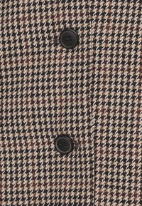 Tissu pied-de-poule marron et beige avec un tissage texturé ; présente deux boutons noirs le long du centre.