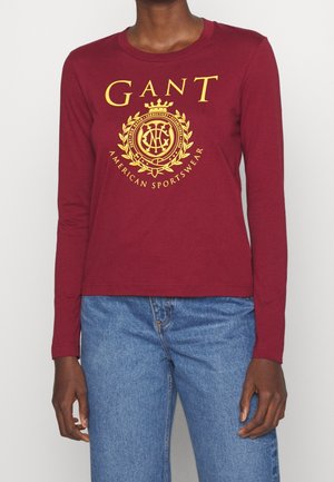 Burgunderfarbener Langarmshirt aus Baumwolle mit großem gelbem Grafiklogo im Kranzdesign auf der Vorderseite. Lässiger Schnitt.