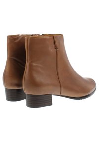 Botas de tobillo de cuero marrón con un acabado suave, un tacón bajo y apilado, y acentos de madera oscura. Cuentan con una cremallera lateral para facilitar su uso.