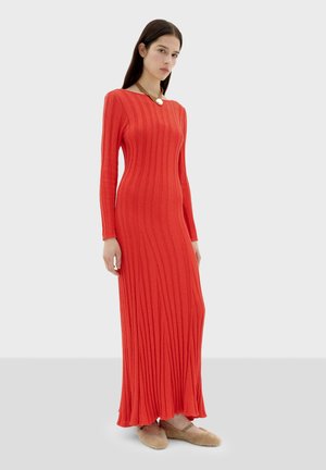 Langsleeve, geribbelde maxi-jurk in levendig rood. Heeft een getailleerde silhoutte met een brede halslijn. Stof lijkt glad en rekbaar.