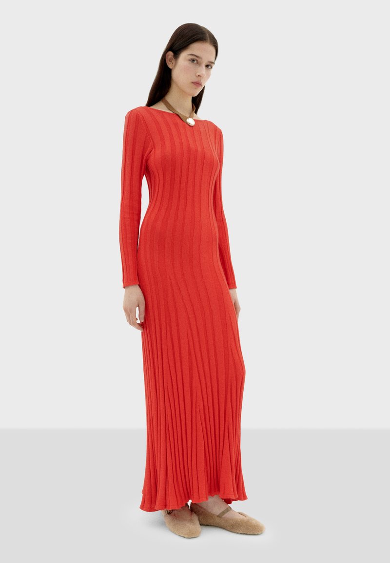 Robe maxi à manches longues et côtelée en rouge vif. Présente une silhouette ajustée avec un décolleté large. Le tissu semble lisse et extensible.