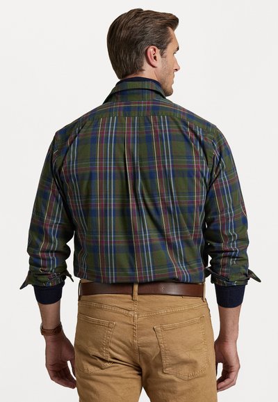 Žalias plaid marškinis su mėlynais ir bordiniais langeliais, mygtukų segtukas ant kaklo ir ilgos rankovės. Dėvima su chaki kelnėmis ir ruduo odiniu diržu.