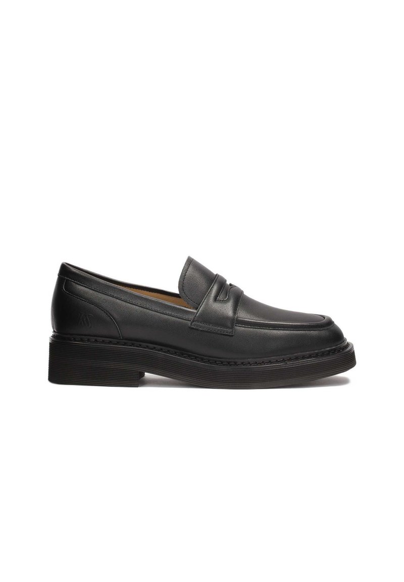 Mocassins en cuir noir avec un bout arrondi, des détails cousus et une semelle en caoutchouc texturée et basse. Dotés d'une lanière à l'avant pour le style.