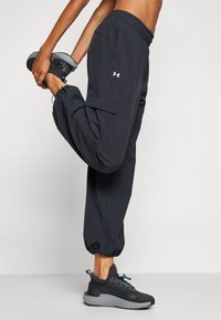 Zwarte sportbroek met een taps toelopende pijp, voorzien van zijzakken en een trekkoord in de taille. Gepaard met donkere sportschoenen.