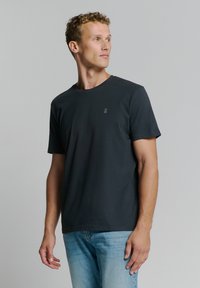 Donkergrijze crew-neck t-shirt van katoen, met korte mouwen en een klein logo op de borst. Gestyled met lichtblauwe jeans.