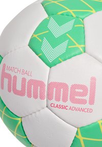 Groene en witte voetbals met een gestructureerd oppervlak, voorzien van een roze logo "hummel CLASSIC ADVANCED" en geometrische patronen in groen en geel.