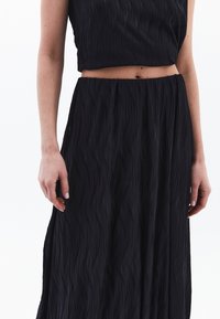 Zwart twee-delig outfit met een getextureerd, golvend ontwerp. De top is cropped met korte mouwen en de rok heeft een vloeiende silhouet.