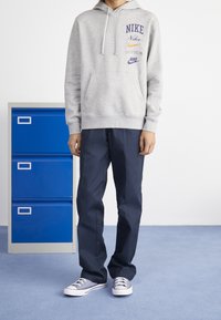 Grå bomullshuvtröja med flera Nike-logotyper, matchad med marinblå byxor och grå kanvas sneakers med vita sulor.