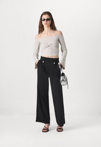 Haut léger gris clair à épaules dénudées avec un design torsadé ; pantalons larges taille haute noirs avec deux accents de boutons argentés ; sandales noires à brides.